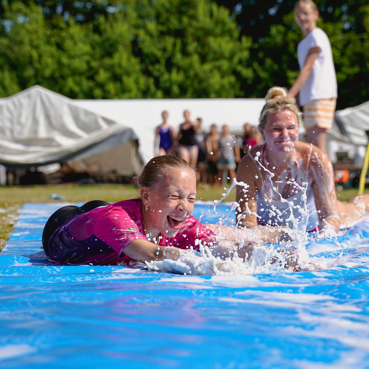 Blondes Mädchen auf Wasserrutsche lachend.