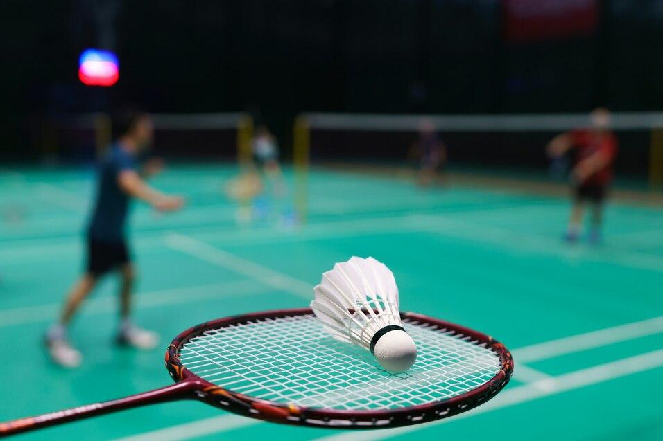 Nahaufnahme eines Badminton-Schl&auml;gers mit Federball auf einem gr&uuml;nen Badmintonplatz im Hintergrund.