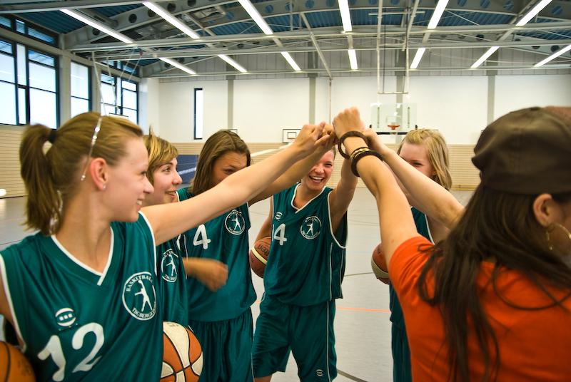 Sechs junge Basketballspielerinnen feiern mit einem Handschlag, w&auml;hrend sie B&auml;lle in ihren H&auml;nden halten.