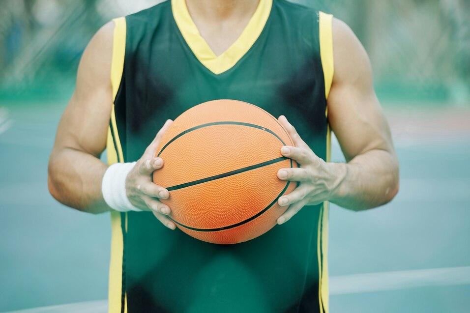 Nahaufnahme eines Basketballspielers, der einen orangefarbenen Basketball in beiden H&auml;nden h&auml;lt.