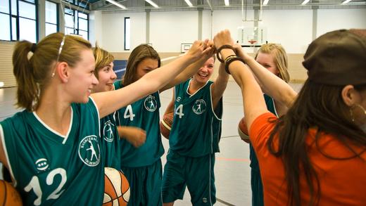 Sechs junge Basketballspielerinnen feiern mit einem Handschlag, w&auml;hrend sie B&auml;lle in ihren H&auml;nden halten.