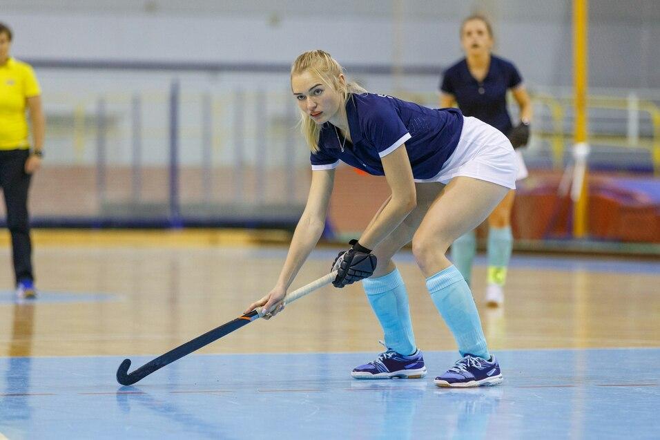 Junge Frau in Sportkleidung h&auml;lt einen Hockeyschl&auml;ger auf einem Hallenboden w&auml;hrend des Trainings.