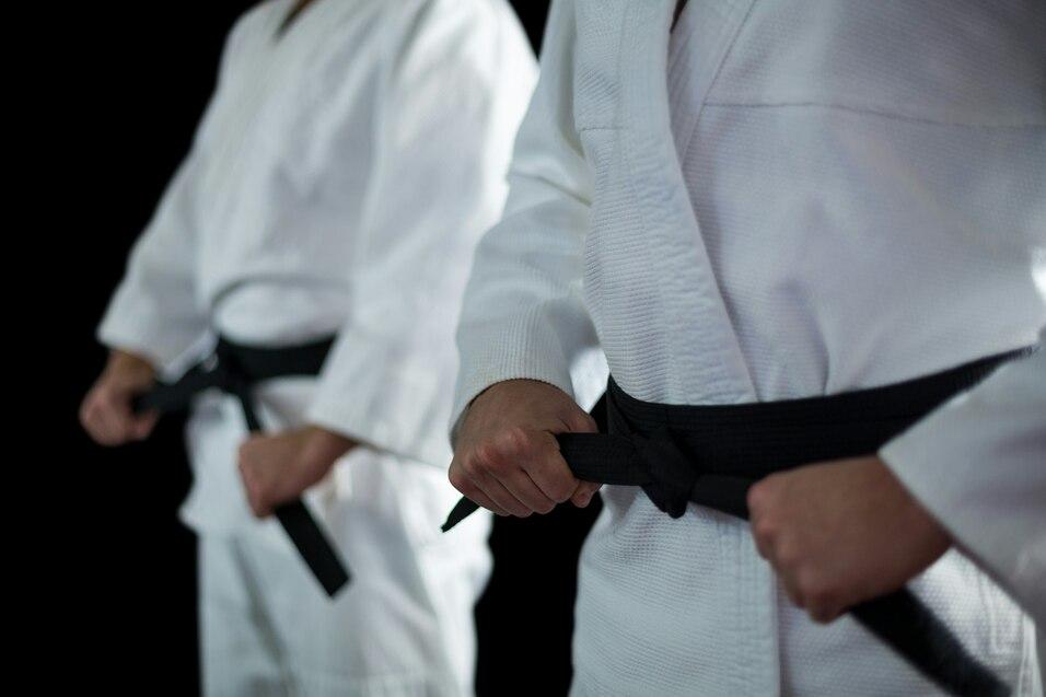 Nahaufnahme von zwei Judokas in wei&szlig;en Anz&uuml;gen mit schwarzen G&uuml;rteln, die an ihren G&uuml;rtelenden ziehen.