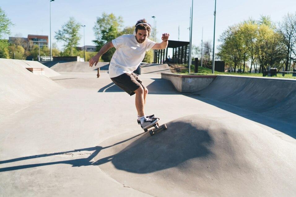 Skateboardfahrer springt &uuml;ber eine kleine Erhebung in einem Skatepark bei sonnigem Wetter.