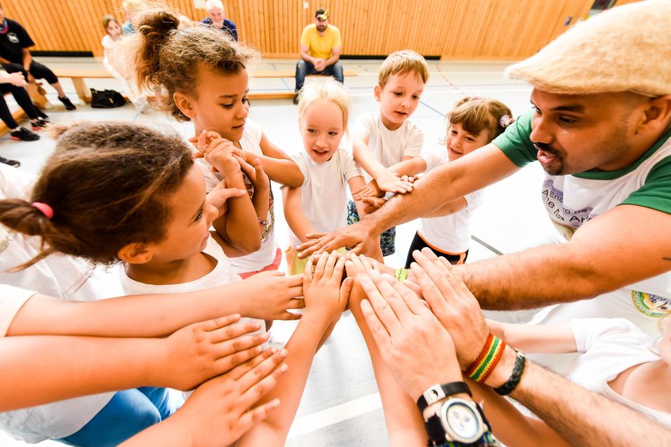 Gruppenspiel mit Kindern, die ihre Hände zum gemeinsamen Aufeinandertreffen heben, unter Anleitung eines Erwachsenen.
