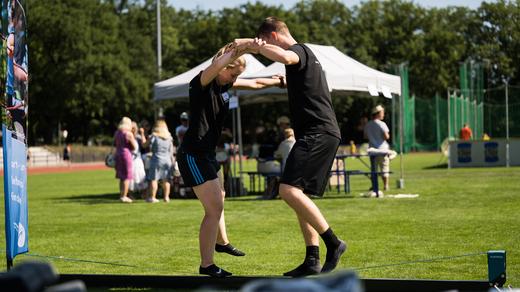 Zwei Personen balancieren auf einem Slackline, umgeben von Zuschauern auf einem Sportplatz.