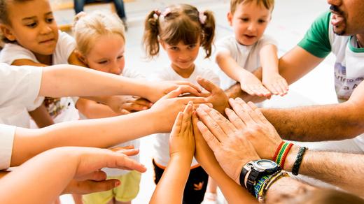 Kinder und Erwachsene legen ihre Hände in einem Kreis zusammen, symbolisieren Zusammenarbeit und Gemeinschaft.