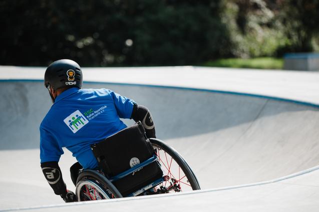 Person im Rollstuhl fährt im Skatepark, trägt einen schwarzen Helm und ein blaues Shirt mit Logo des RSC Rheinhessen.