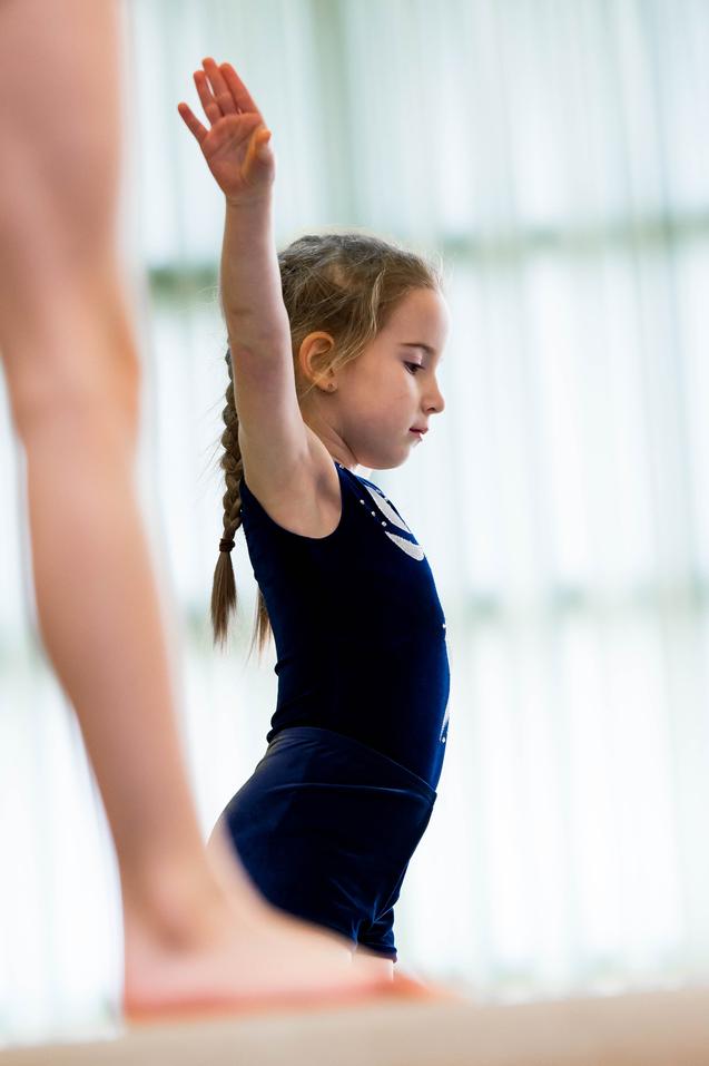 Mädchen mit geflochtenem Haar in blauem Trainingsanzug hebt den Arm und konzentriert sich während des Turntrainings.