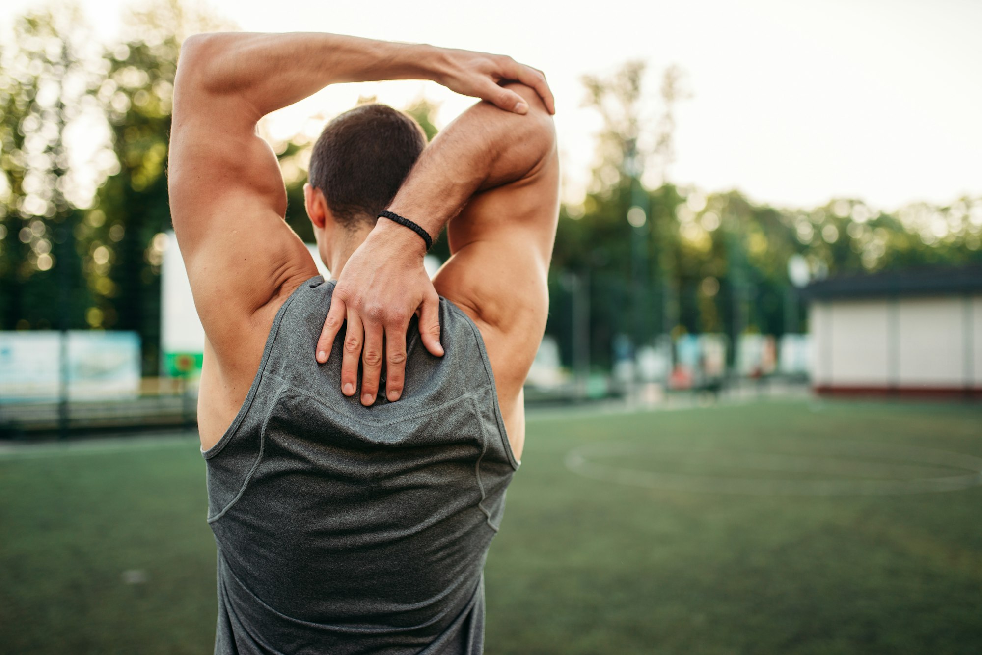 Male athlete doing stretching exercise, back view