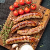 Fried sausages with sauces and herbs on a wooden serving Board. Great beer snack on a dark background. Top view.