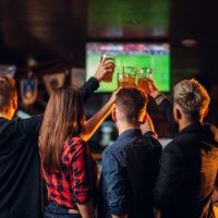 Fun friends watches football on TV and raised their glasses with beer in a sport bar, happy fans, celebration of the victory in game